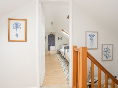 A hallway with a view into a bedroom and bathroom with blue tiled wall beside a wooden staircase with marine-themed artwork on the walls at The Palms in Abersoch
