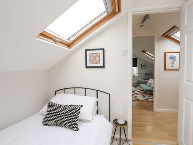 A small bedroom with a single bed under a skylight window and a small round bedside table at The Palms in Abersoch