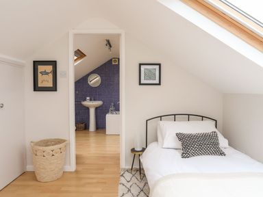 A bedroom with a bed side table and wall decorations leading to a bathroom with a sink and blue tiled wall at The Palms in Abersoch