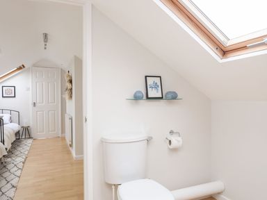 A bathroom with a toilet beneath a skylight and a shelf with decorative items next to a bedroom at The Palms in Abersoch