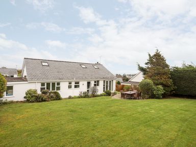 A white house with a grey roof and garden furniture on a patio beside a lawn at The Palms in Abersoch