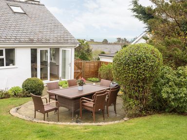 An outdoor patio with a rectangular table and six chairs surrounded by bushes and grass at The Palms in Abersoch
