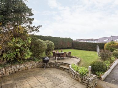 A garden with a patio table and chairs a barbecue and stone walls at The Palms in Abersoch