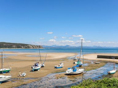 Boats resting on a sandy beach with water channels and hills in the background at The Palms in Abersoch