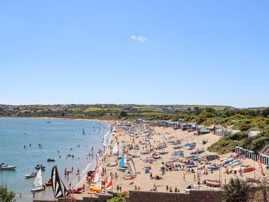 A beach with many people boats and colorful tents along the shore at The Palms in Abersoch