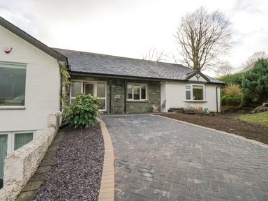 A driveway leading to a single-story house with a stone and white exterior at Whimhowe in Windermere