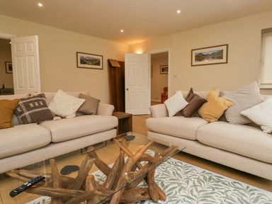 A living room with two beige sofas and a glass coffee table with wooden base at Whimhowe in Windermere