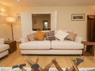 A living room with a beige sofa with cushions and wooden side tables at Whimhowe in Windermere
