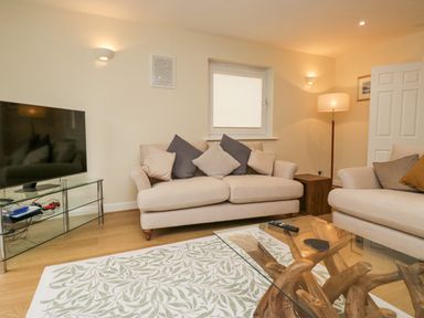 A living room with two beige sofas and a glass coffee table on a patterned rug at Whimhowe in Windermere