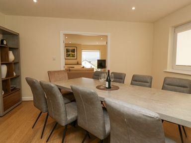 A dining room with a large table surrounded by chairs and a bottle of wine with wine glasses at Whimhowe in Windermere