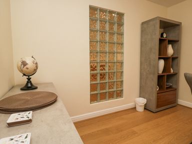 A corner of a room with a globe on a countertop next to round placemats a tall shelving unit with decorative items and a small trash bin on a wooden floor at Whimhowe in Windermere