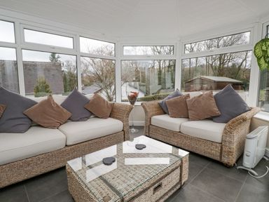 A conservatory with two wicker sofas with cushions and a wicker coffee table with a glass top at Whimhowe in Windermere
