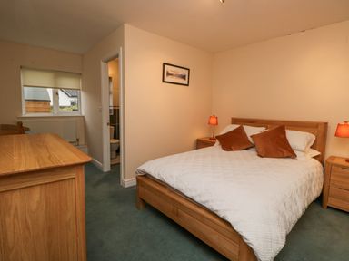 A bedroom with a wooden bed and bedside tables with lamps and a window with a blind at Whimhowe in Windermere