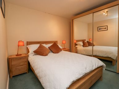 A bedroom with a wooden bed two brown pillows white bedding two bedside tables with lamps and mirrored wardrobe at Whimhowe in Windermere