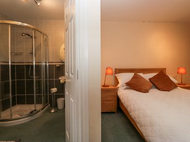 A bedroom with a double bed and two bedside tables with lamps next to an en suite shower room at Whimhowe in Windermere