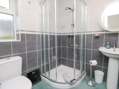 A bathroom with a corner shower enclosure a toilet a pedestal sink a round mirror and a digital scale on the floor at Whimhowe in Windermere