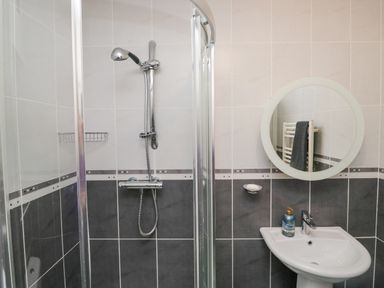 A bathroom with a corner shower enclosure a round mirror and a pedestal sink at Whimhowe in Windermere