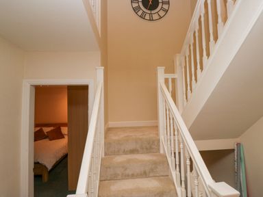 A staircase with beige carpet and white railing with a doorway showing a bedroom with pillows at Whimhowe in Windermere
