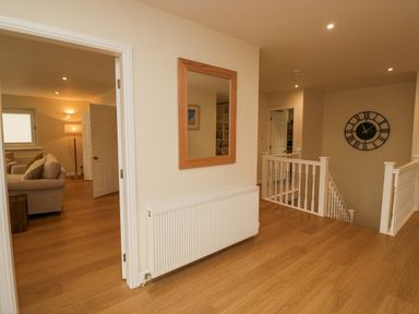 A hallway with wooden floor a wall mirror and radiator a wall clock and a staircase at Whimhowe in Windermere