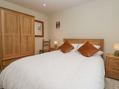 A bedroom with a wooden bed with white bedding and brown pillows a wooden wardrobe two bedside tables with lamps and a wooden chair at Whimhowe in Windermere