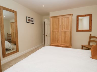 A bedroom with a wooden wardrobe chair wall mirror and a full length mirror at Whimhowe in Windermere