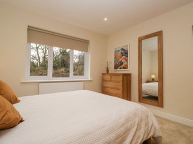A bedroom with a bed white blanket pillows wooden chest of drawers and a tall wooden mirror at Whimhowe in Windermere