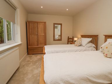 A bedroom with two single beds with white bedding a wooden wardrobe a chair a mirror and a window at Whimhowe in Windermere