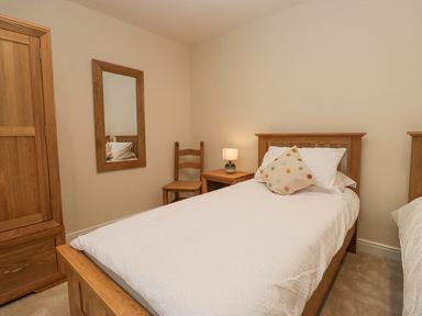 A bedroom with two single beds a wooden chair a bedside table with a lamp a wooden wardrobe and a wall mirror at Whimhowe in Windermere