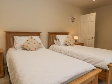 A bedroom with two single wooden beds white bedding and polka dot cushions at Whimhowe in Windermere