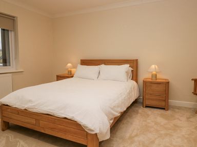 A bedroom with a wooden bed frame white bedding two wooden nightstands with lamps and a window at Whimhowe in Windermere