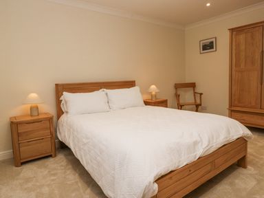 A bedroom with a double bed white bedding two wooden nightstands with lamps a wooden chair and a wooden wardrobe at Whimhowe in Windermere