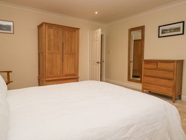 A bedroom with a wooden wardrobe wooden chest of drawers wall mirror and a bed with white bedding at Whimhowe in Windermere