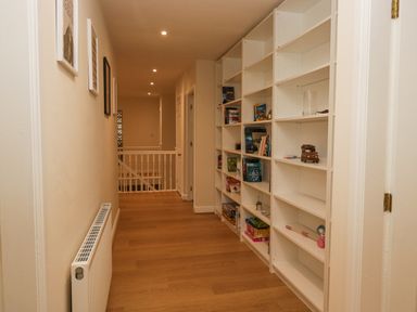 A hallway with wooden floor a white radiator and bookshelves along one wall at Whimhowe in Windermere
