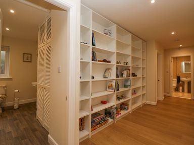 A hallway with white shelves holding books and games with doors leading to bathrooms at Whimhowe in Windermere