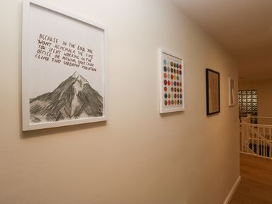 A hallway with framed pictures on a wall and a white railing near the stairs at Whimhowe in Windermere