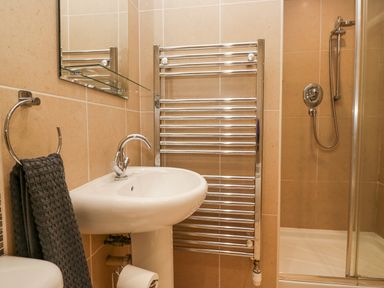 A bathroom with a sink a towel rack a shower and a towel hanging on a ring at Whimhowe in Windermere