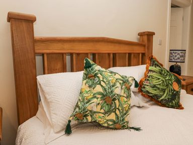 A bed with wooden headboard white bedding and decorative pillows with botanical prints at Whimhowe in Windermere