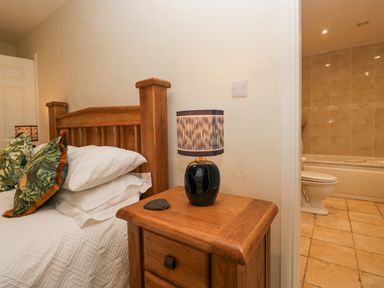 A wooden bed with pillows and a bedside table with a lamp next to a bathroom with a toilet and bathtub at Whimhowe in Windermere