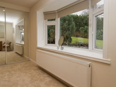 A room with a window showing greenery outside a radiator below the window and a mirror on the window sill at Whimhowe in Windermere
