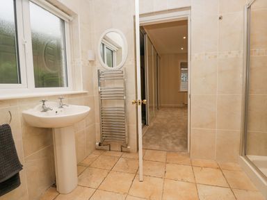 A bathroom with a pedestal sink towel rack mirror and shower next to a door opening to a carpeted room at Whimhowe in Windermere