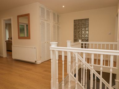 A hallway with wooden floor, white stair railing, built-in closets, a wall mirror and a glass block window at Whimhowe in Windermere