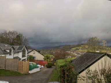 A residential street with houses trees and hills under cloudy sky at Whimhowe in Windermere