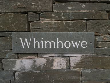 A slate nameplate with the inscription Whimhowe mounted on a stone wall at Whimhowe in Windermere