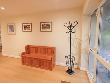 An entryway with a wooden bench a black metal coat rack three framed pictures on a wall and a glass door at Whimhowe in Windermere