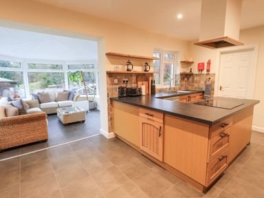 A kitchen with wooden cabinets and a black countertop next to a seating area with wicker sofas and a coffee table at Whimhowe Windermere