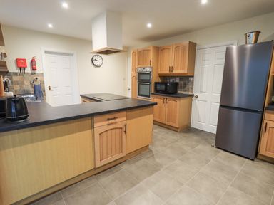 A kitchen with wooden cabinets a black countertop a refrigerator and a microwave at Whimhowe in Windermere