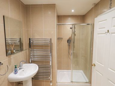 A bathroom with a white sink, chrome towel rack, mirror, and glass-enclosed shower at Whimhowe in Windermere