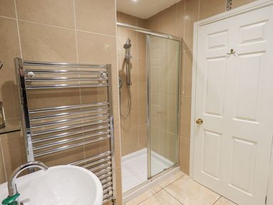 A bathroom with a shower enclosure a white door a towel radiator and a sink at Whimhowe in Windermere
