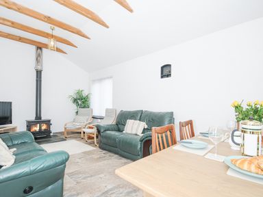 A living room with green leather sofas a wood stove two armchairs and a dining table set with plates and croissants at The Dairy Barn in Camelford