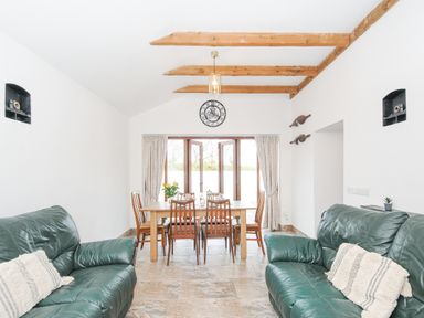 A dining room with a wooden table and chairs between two green leather sofas at The Dairy Barn in Camelford